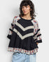Woman wearing a black sweater with colorful patterns and tassels on a white background