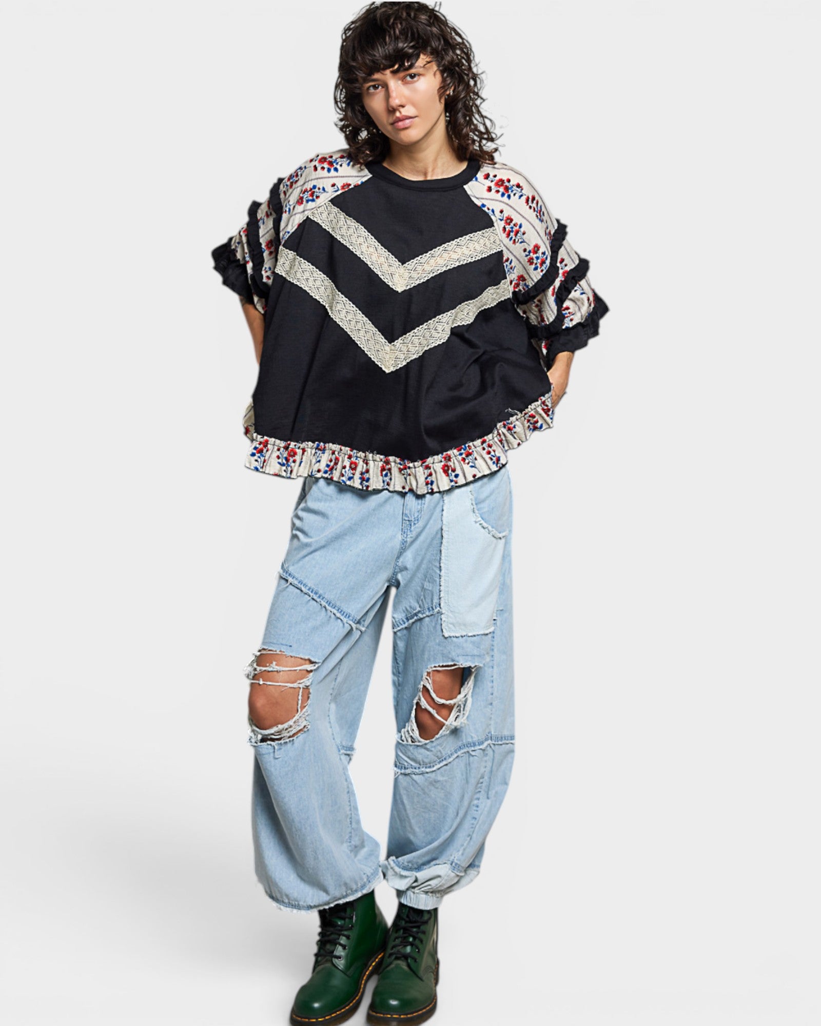 Person wearing a black and floral sweater with ripped jeans on a white background