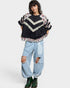 Person wearing a black and floral sweater with ripped jeans on a white background