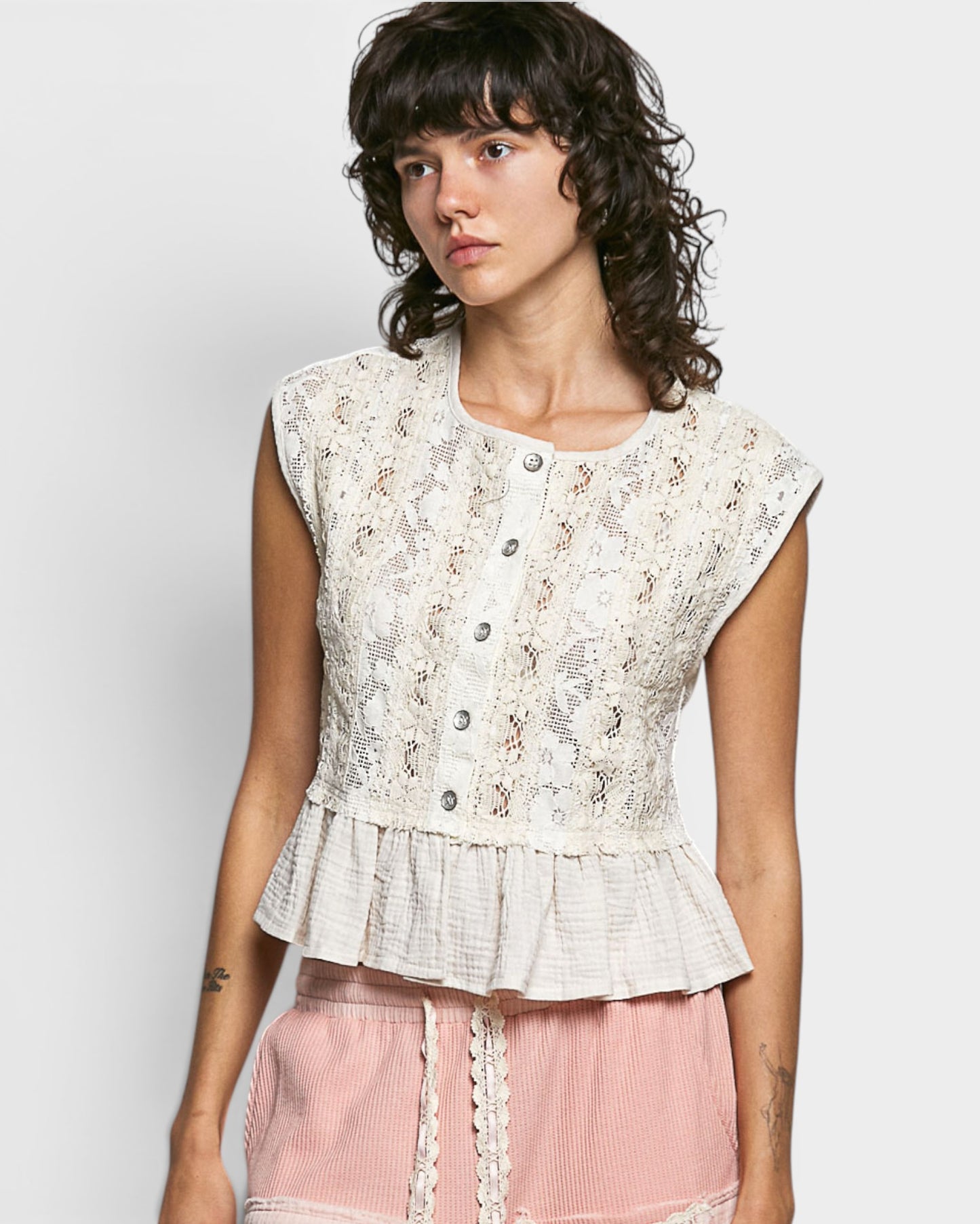 Woman wearing a sleeveless lace top with a plain background