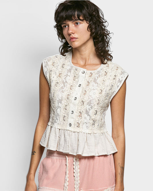 Woman wearing a sleeveless lace top with a plain background
