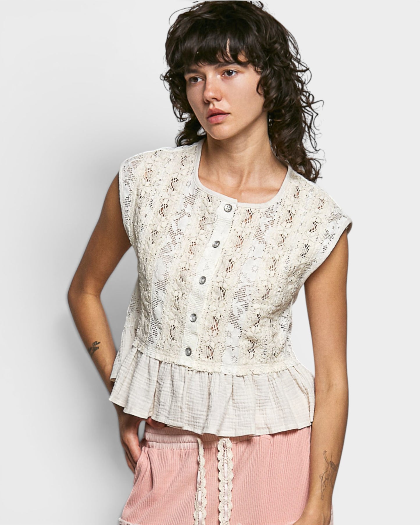 Woman wearing a floral peplum top and pink pants against a white background