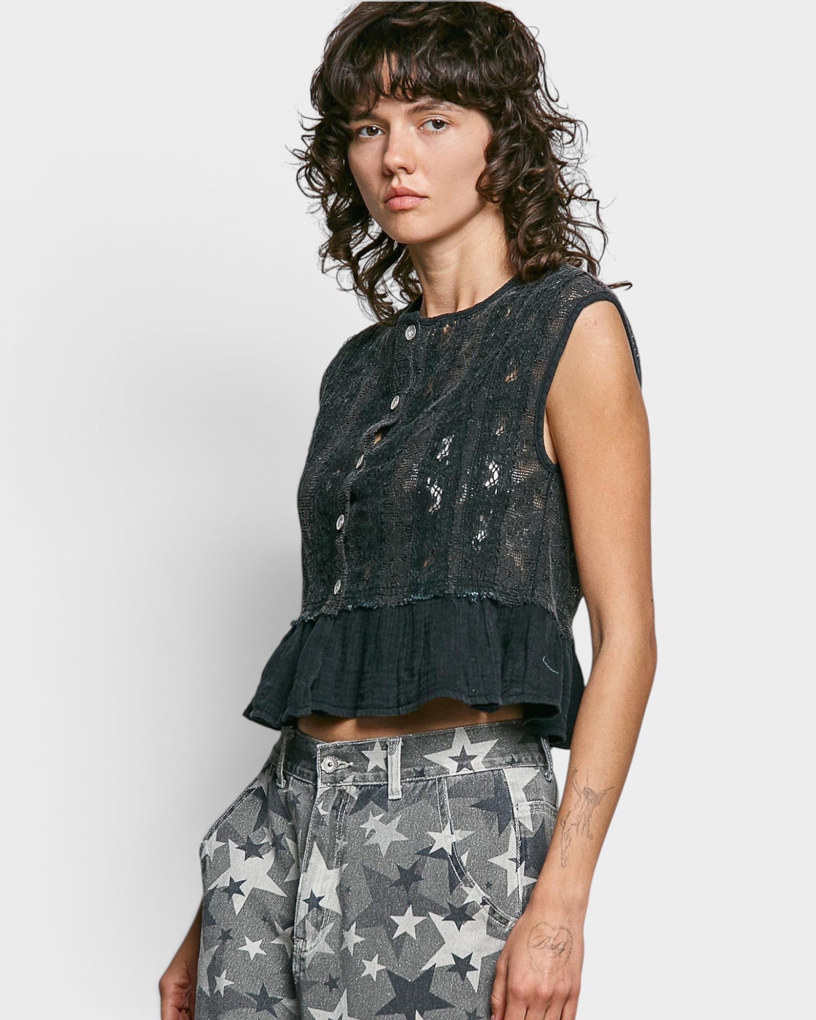 Woman wearing a dark sleeveless top with star patterns on a light gray background