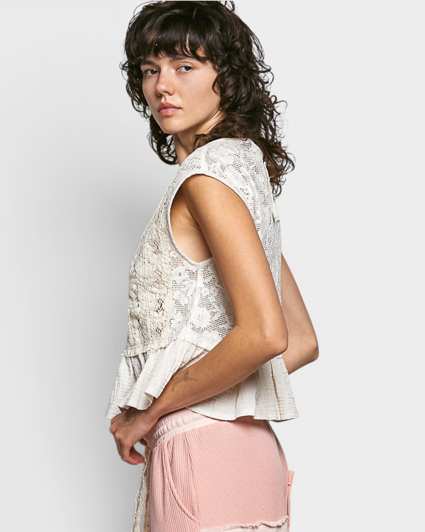 Woman wearing a light-colored sleeveless top and pink pants on a plain background