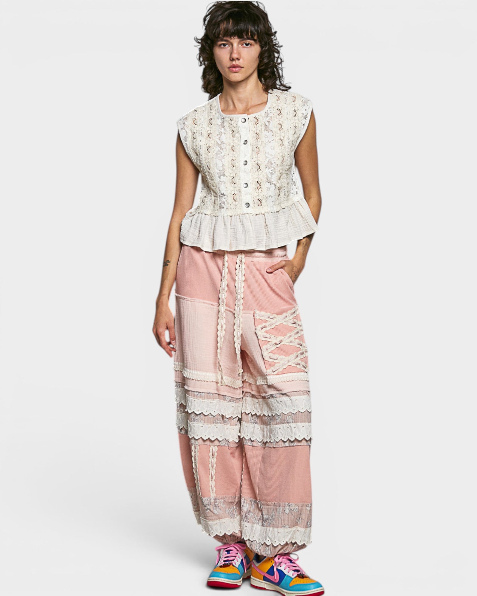 Woman wearing a white lace top and pink lace pants on a white background