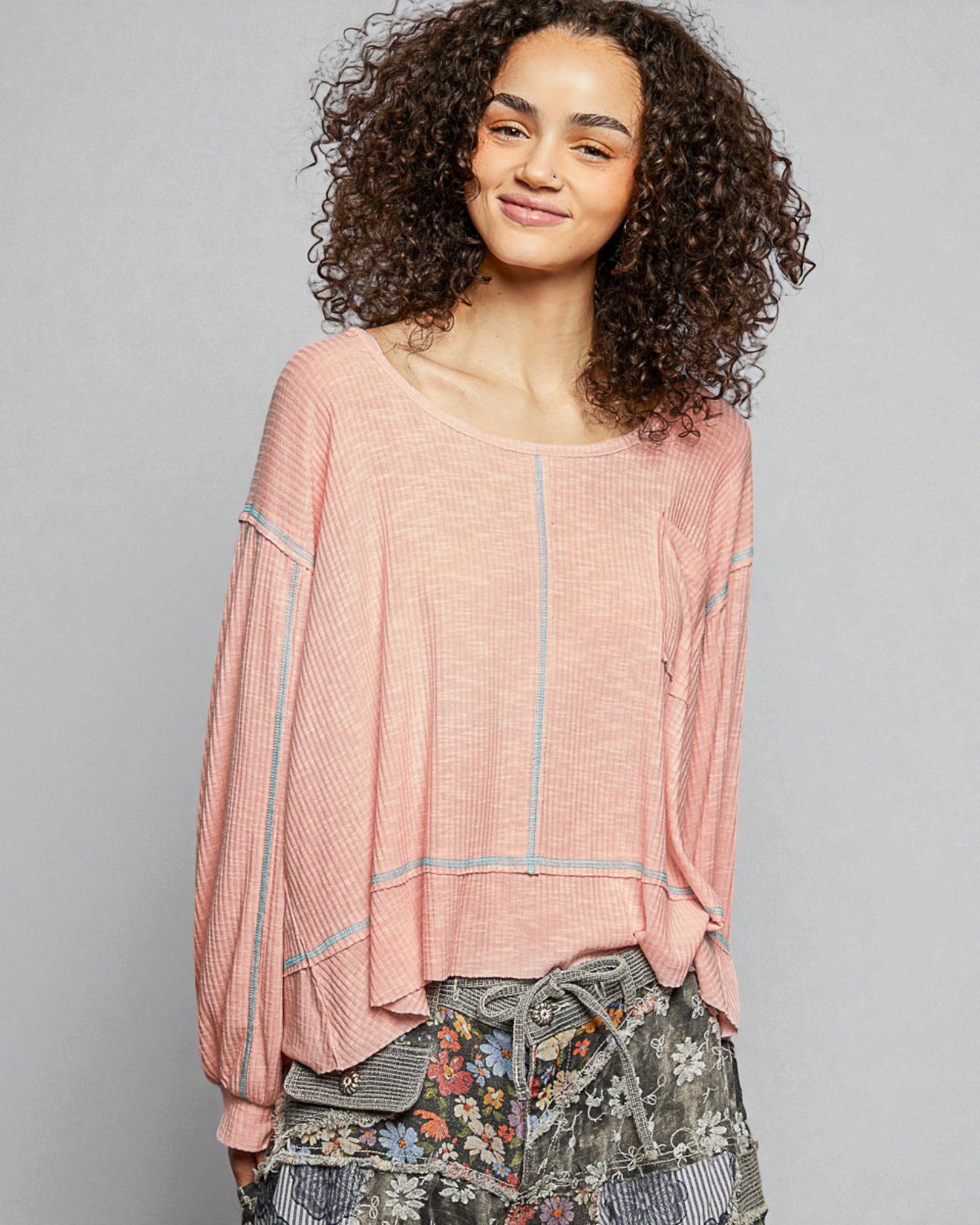 Woman wearing a pink top with floral pants against a gray background