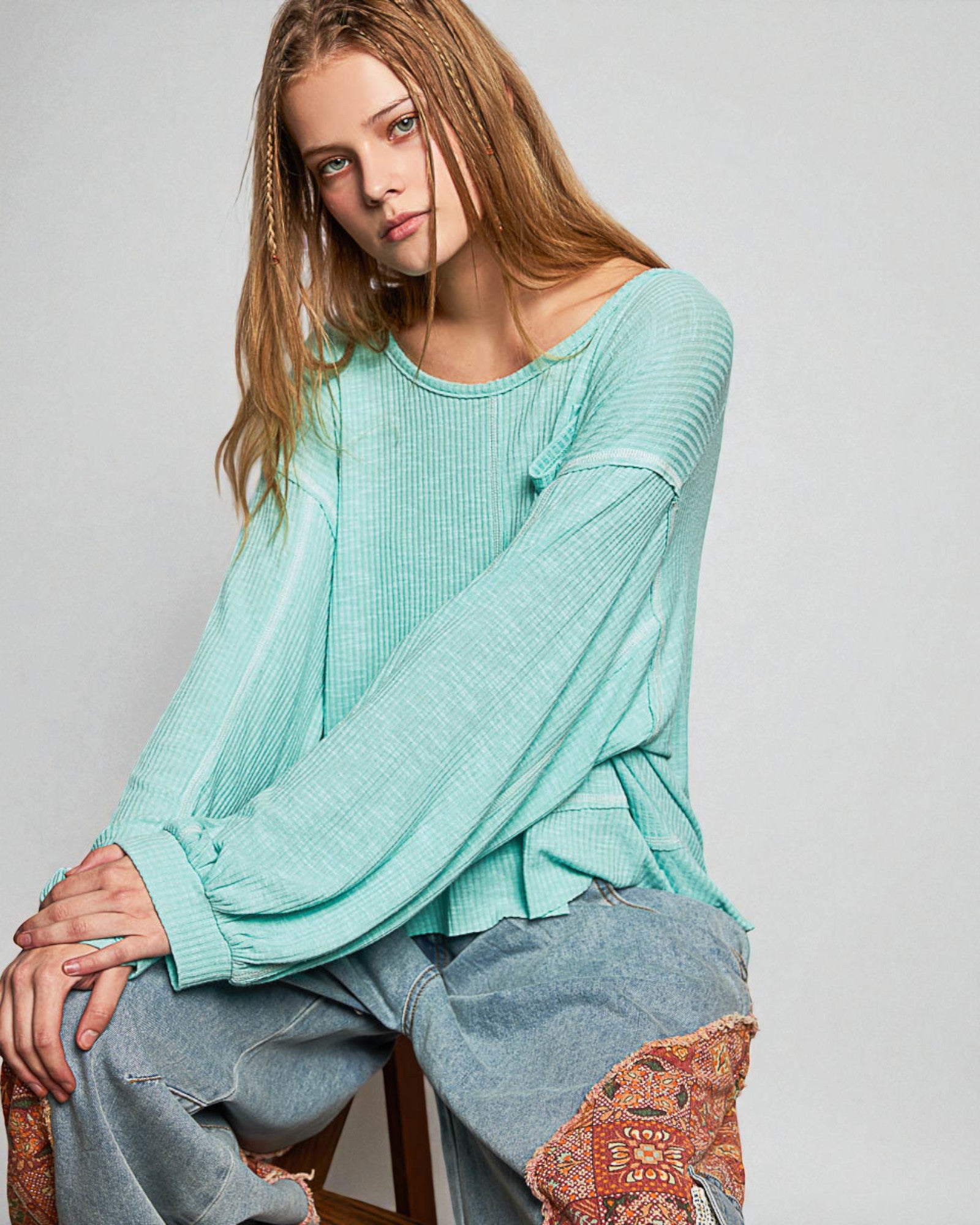 Woman wearing a light blue sweater and jeans sitting on a chair with a patterned cushion.