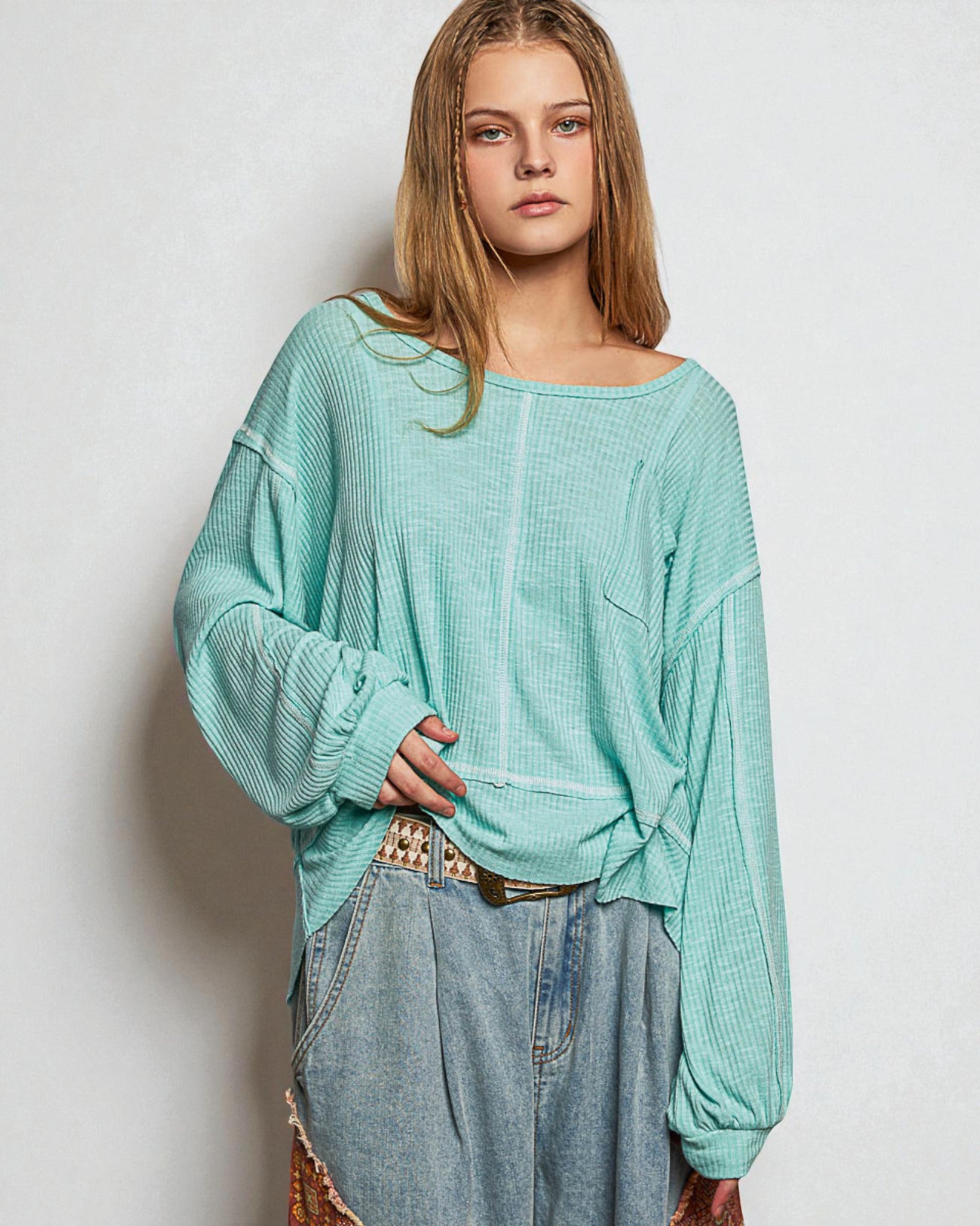 Woman wearing a light blue textured top and jeans against a plain background