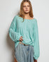 Woman wearing a light blue textured top and jeans against a plain background