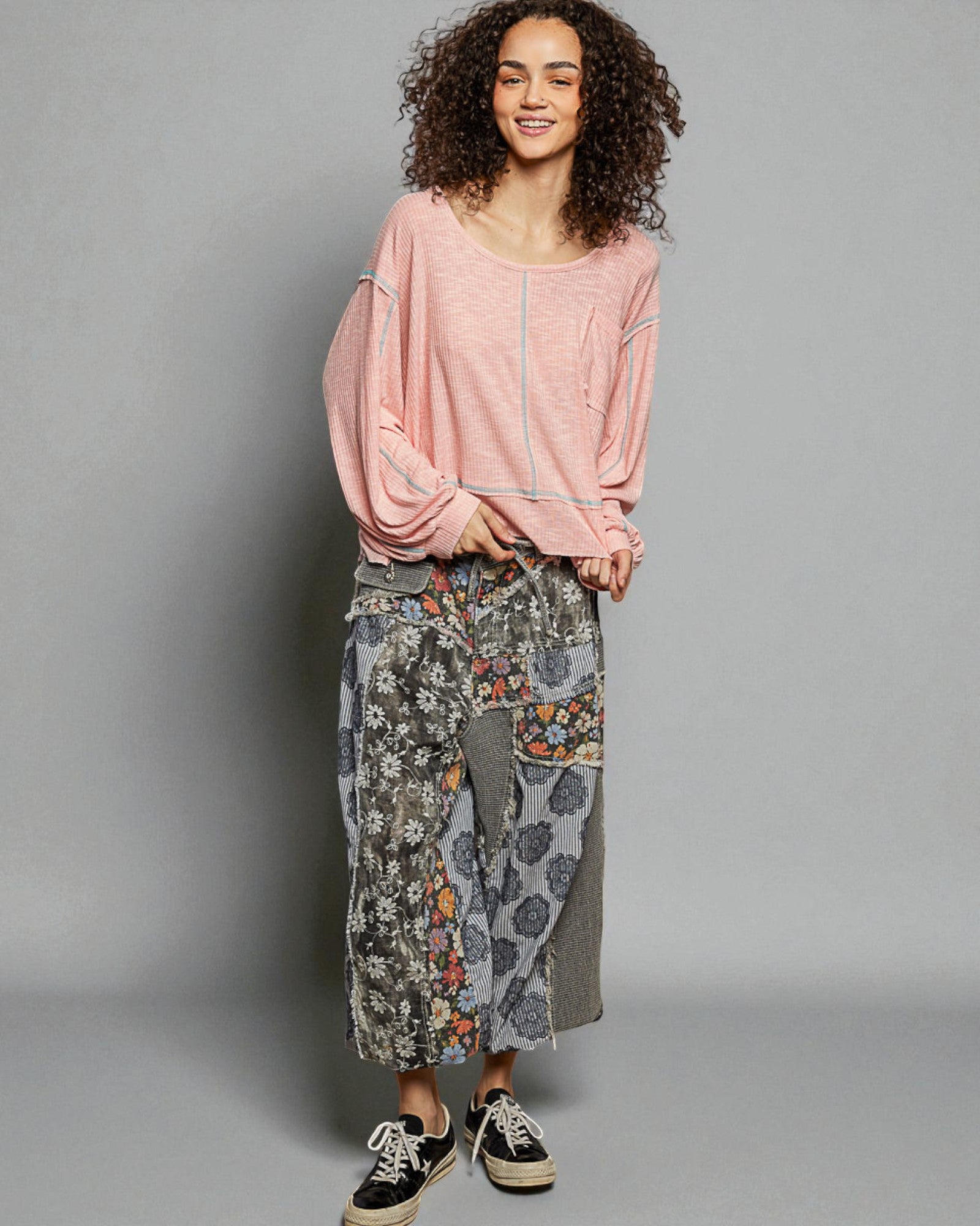 Woman wearing a pink top and patterned pants on a gray background