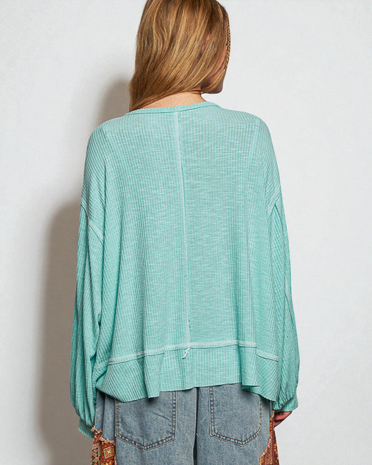 Person wearing a teal long-sleeve top against a plain background