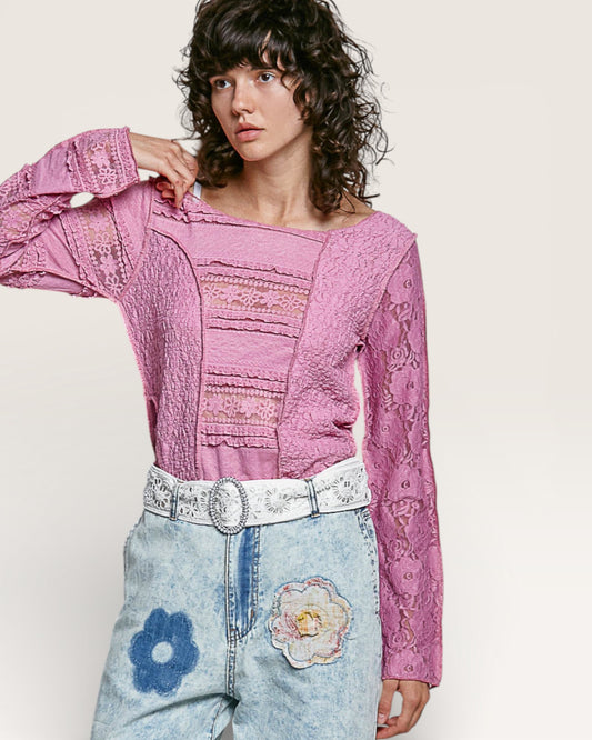 Person wearing a pink lace top and light blue jeans with floral patches on a white background