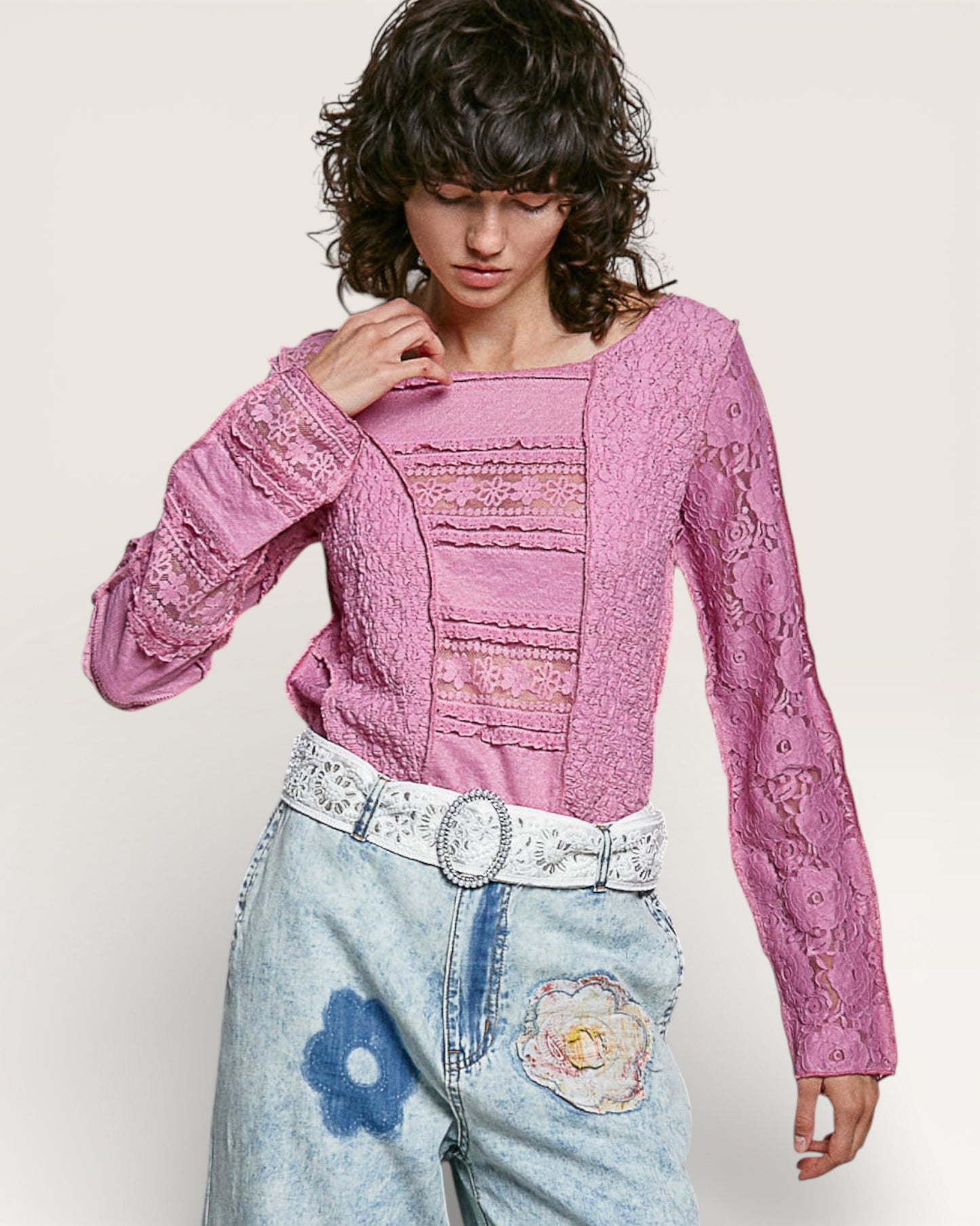 Woman wearing a pink lace top and floral jeans on a white background
