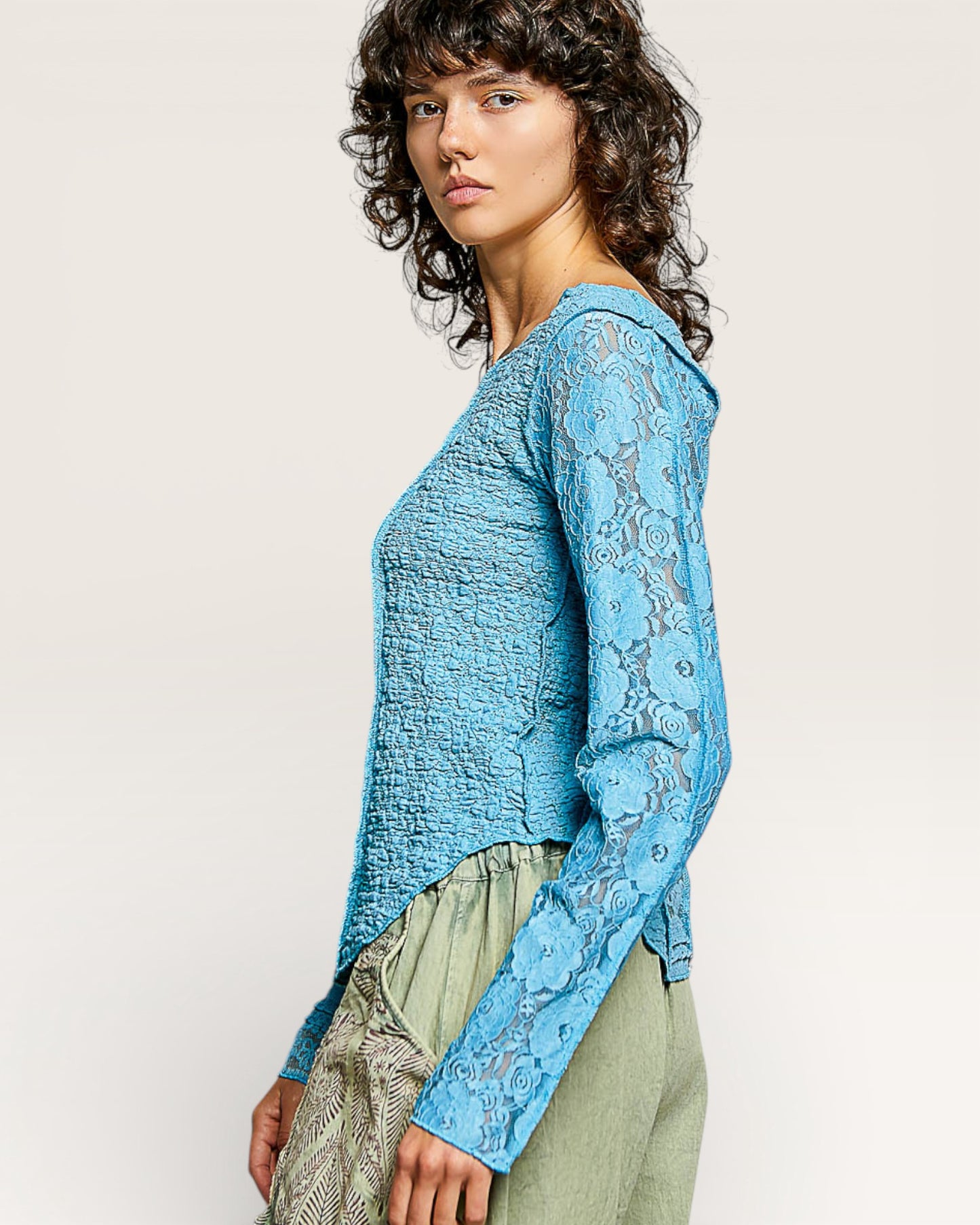 Woman wearing a blue lace top with a plain background