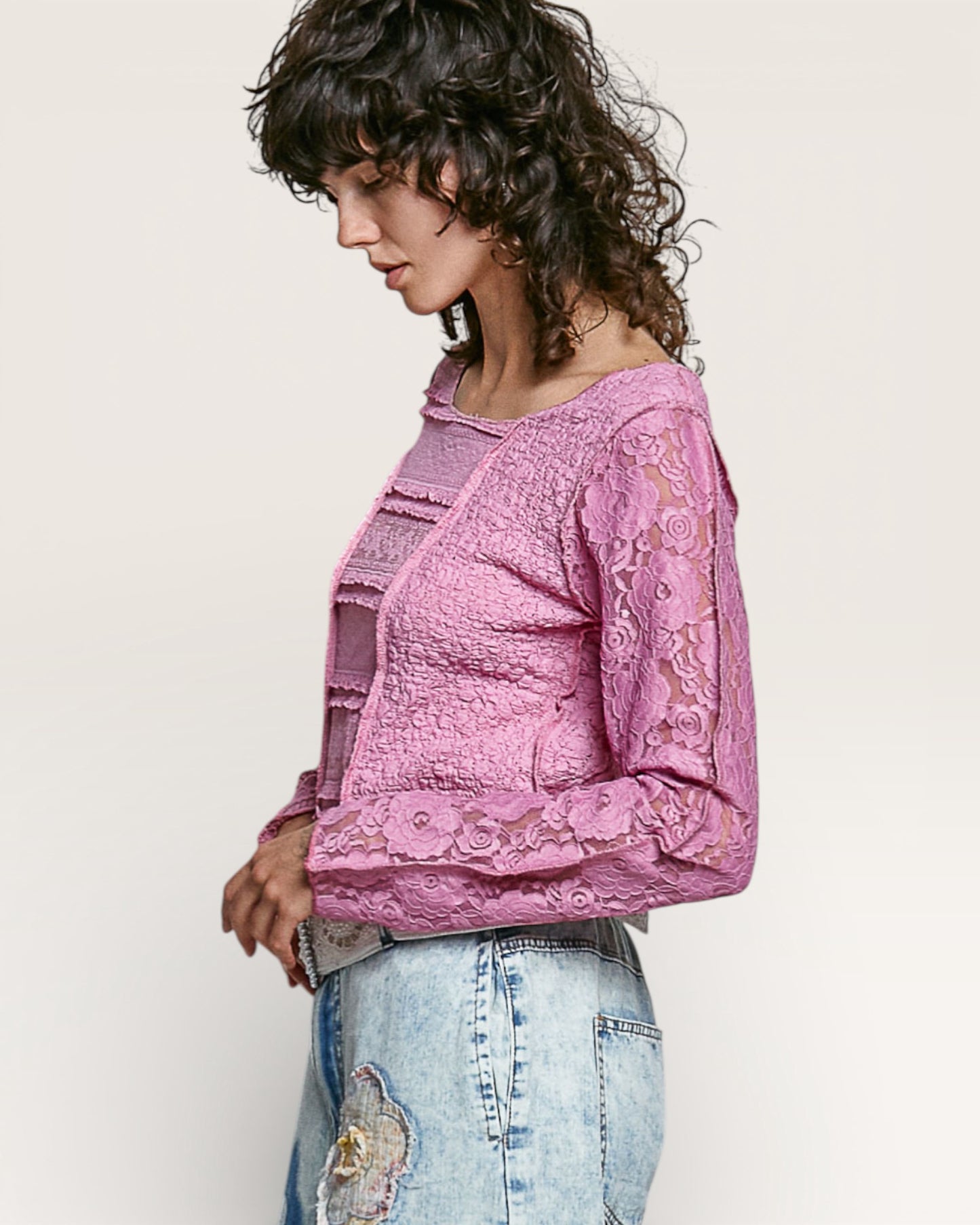 Woman wearing a pink lace top and light blue jeans on a plain background