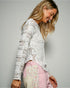 Woman wearing a white lace top and pink pants against a gray background