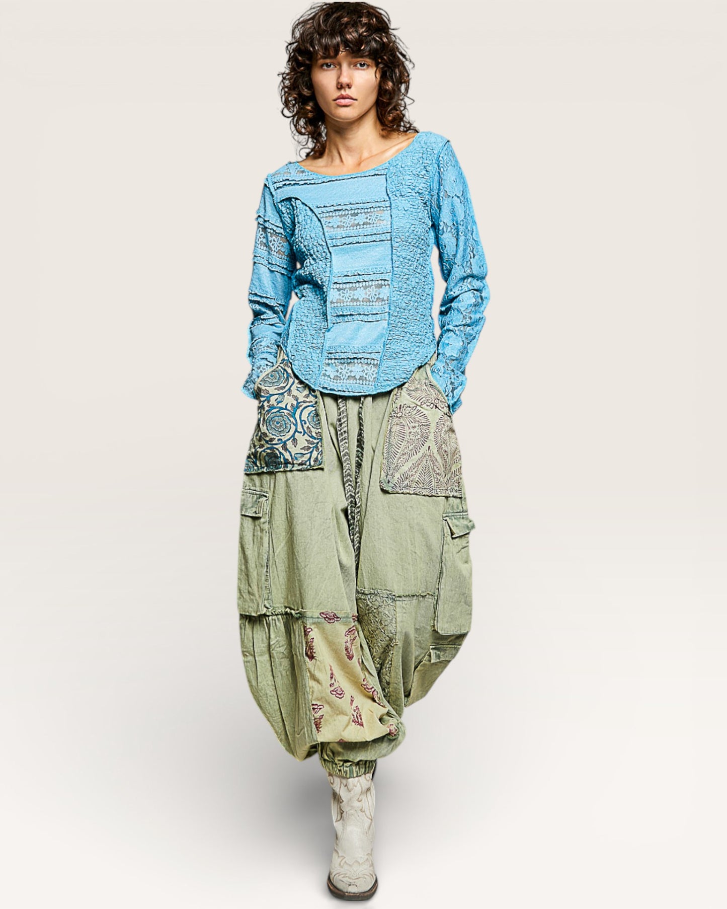 Person wearing a blue patterned sweater and green harem pants on a white background