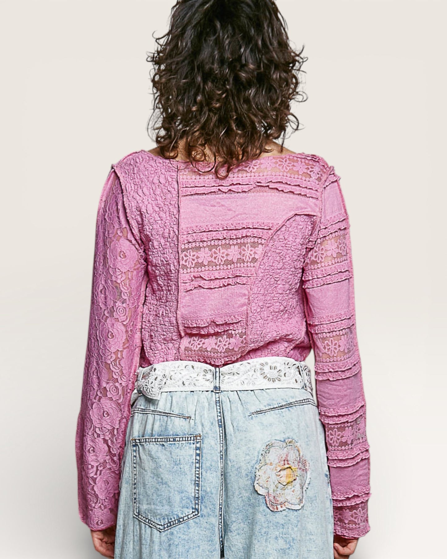 Person wearing a pink lace top and light blue jeans with a white background