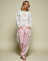 Woman wearing a white patterned top and pink pants against a beige background
