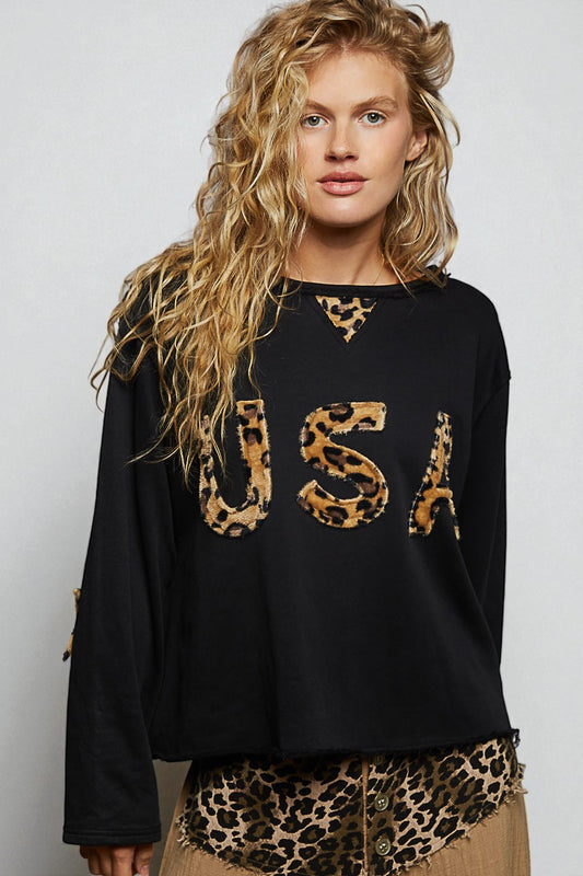 Woman wearing a black sweater with leopard print letters on a plain background