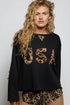 Woman wearing a black sweater with leopard print letters on a plain background