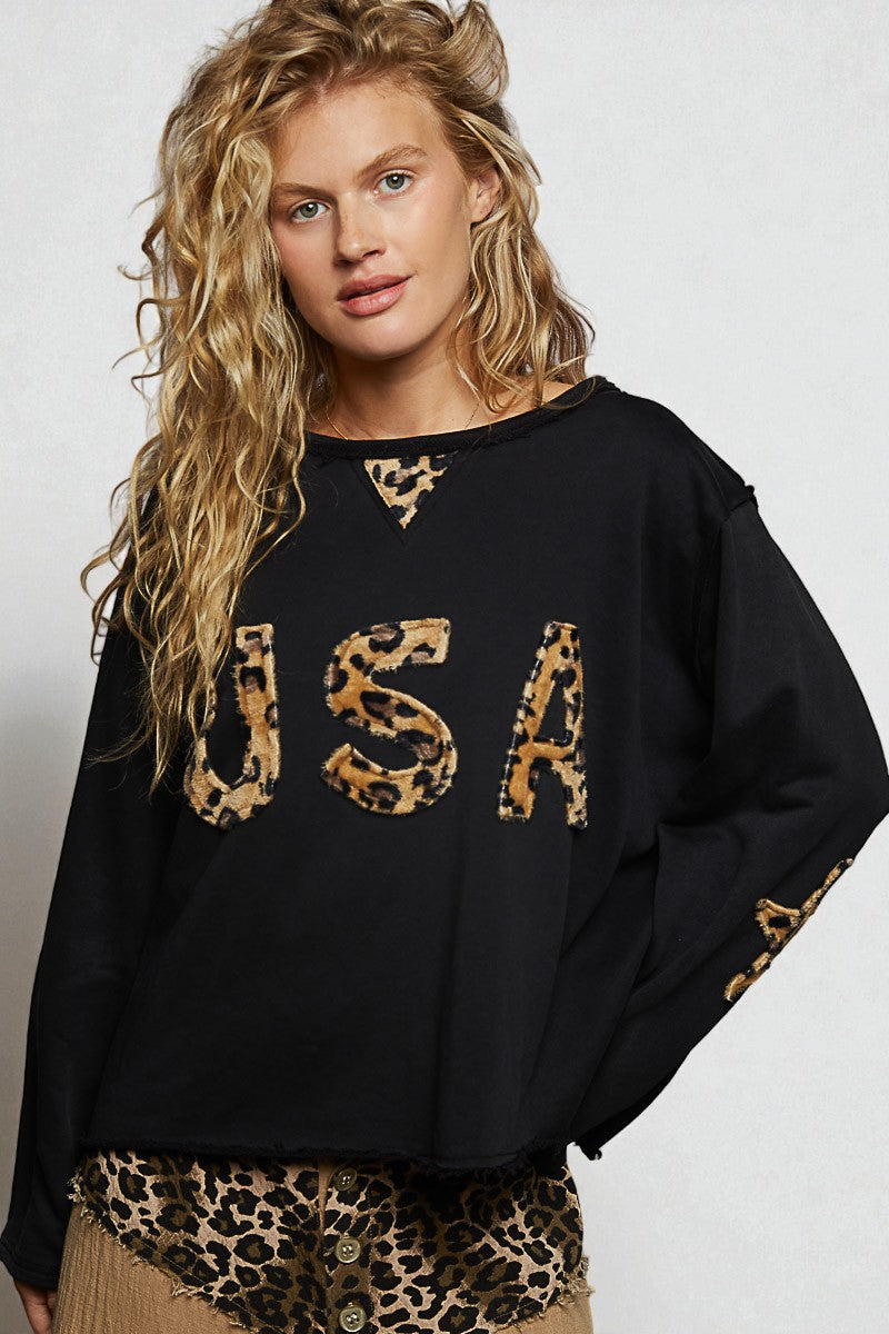 Woman wearing a black sweater with leopard print 'USA' letters on a white background