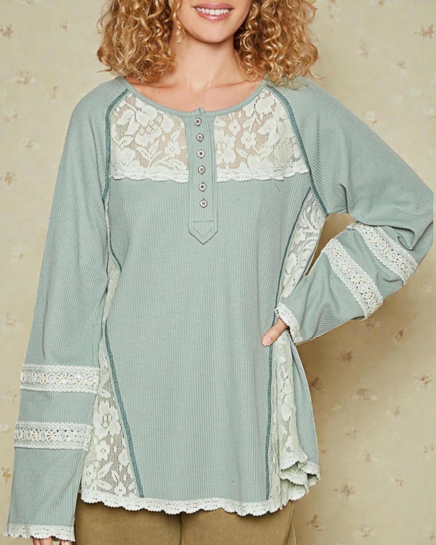 Woman wearing a light blue long-sleeve top with lace details on a beige background