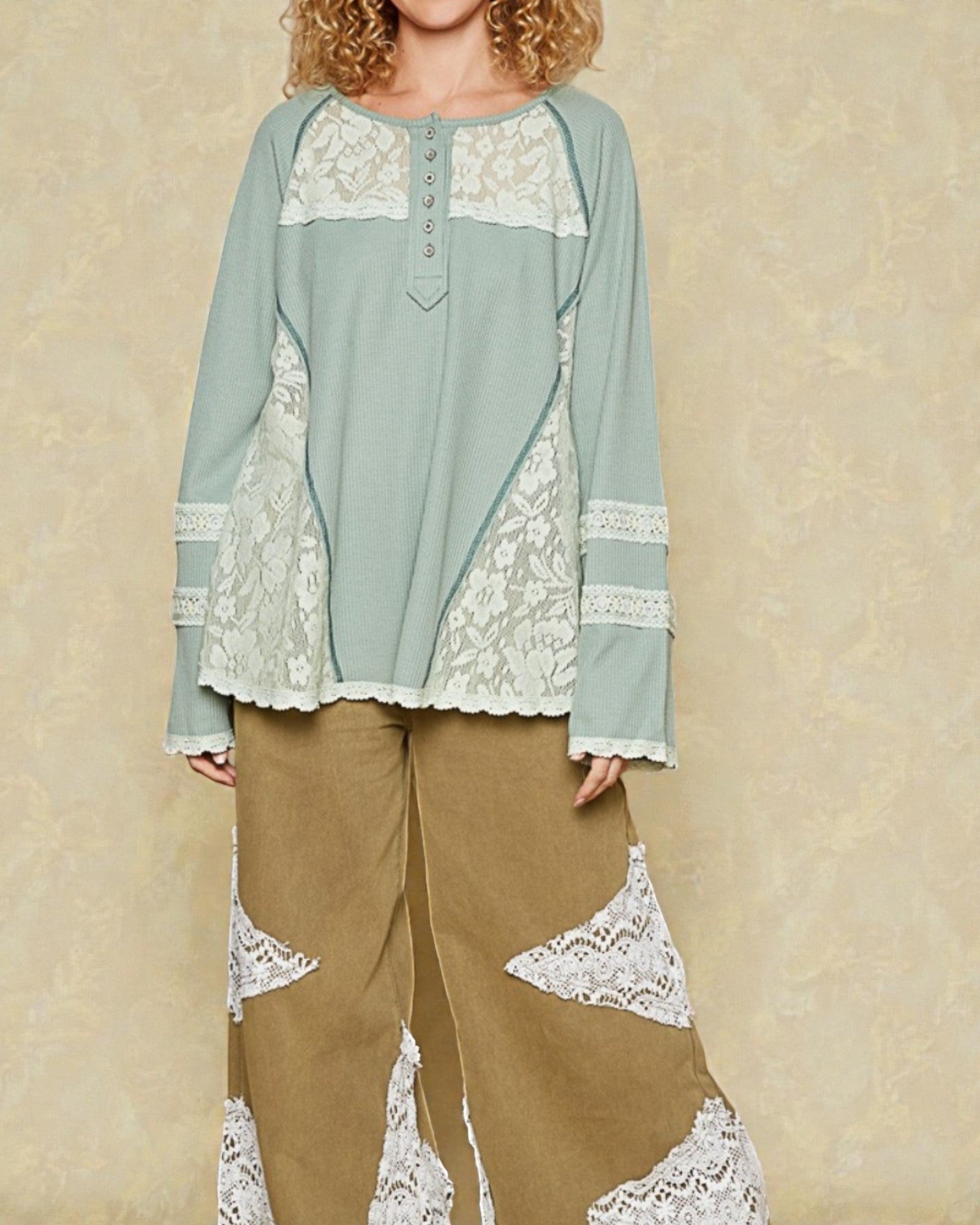 Woman wearing a light blue top and brown pants with lace details against a beige background
