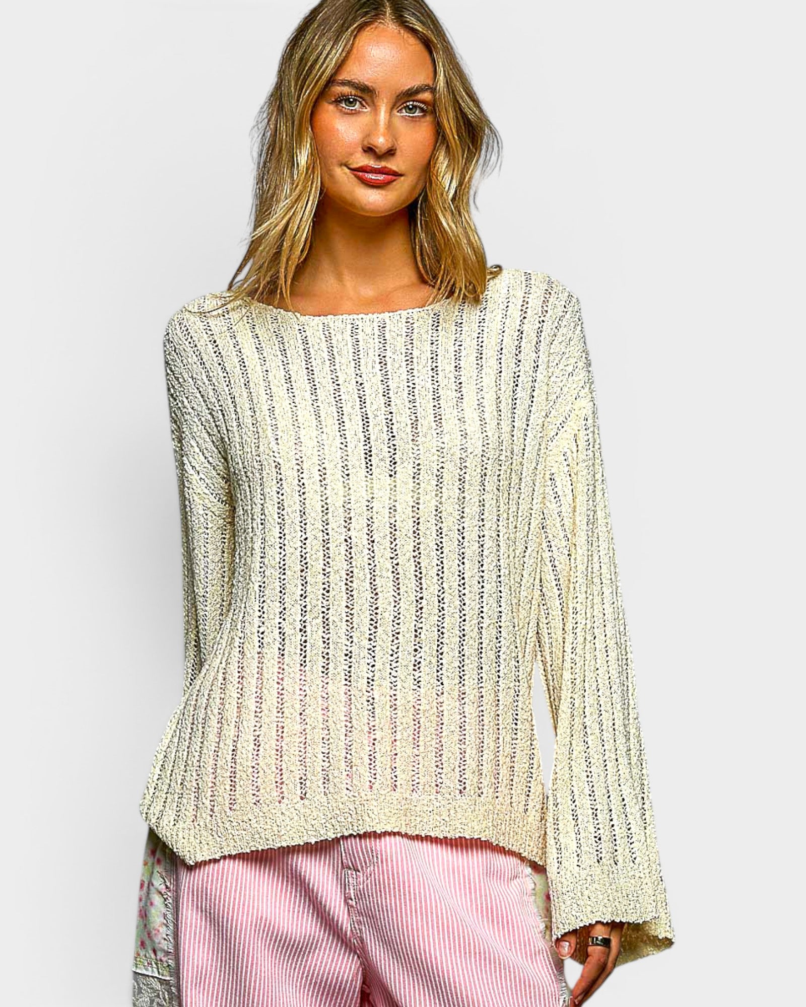 Woman wearing a light-colored knit sweater and pink pants on a white background