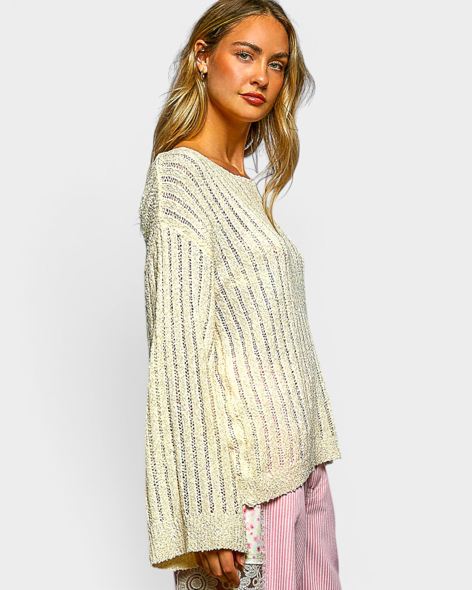 Woman wearing a light-colored knit sweater and pink pants on a plain background