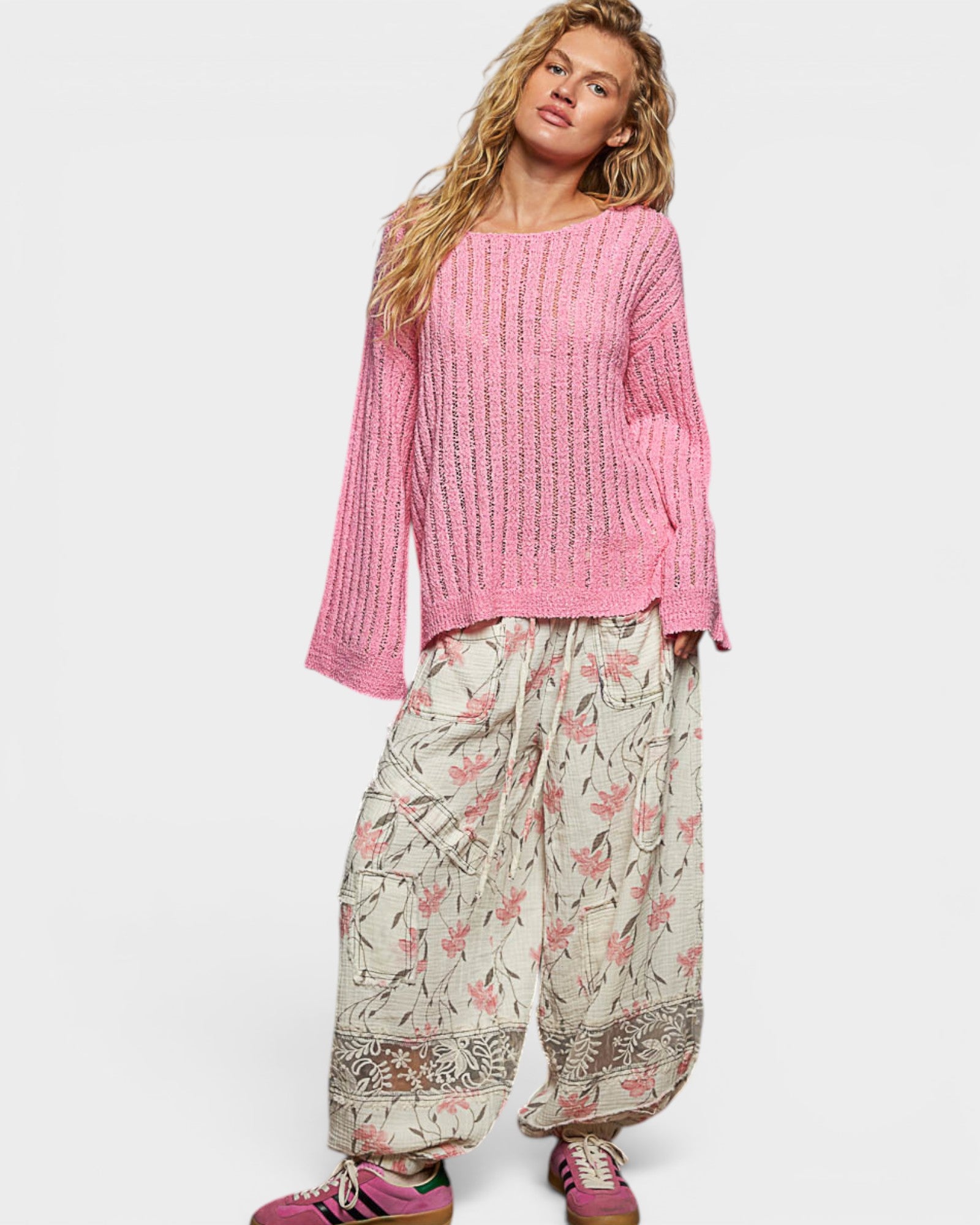 Woman wearing a pink sweater and floral pants on a white background