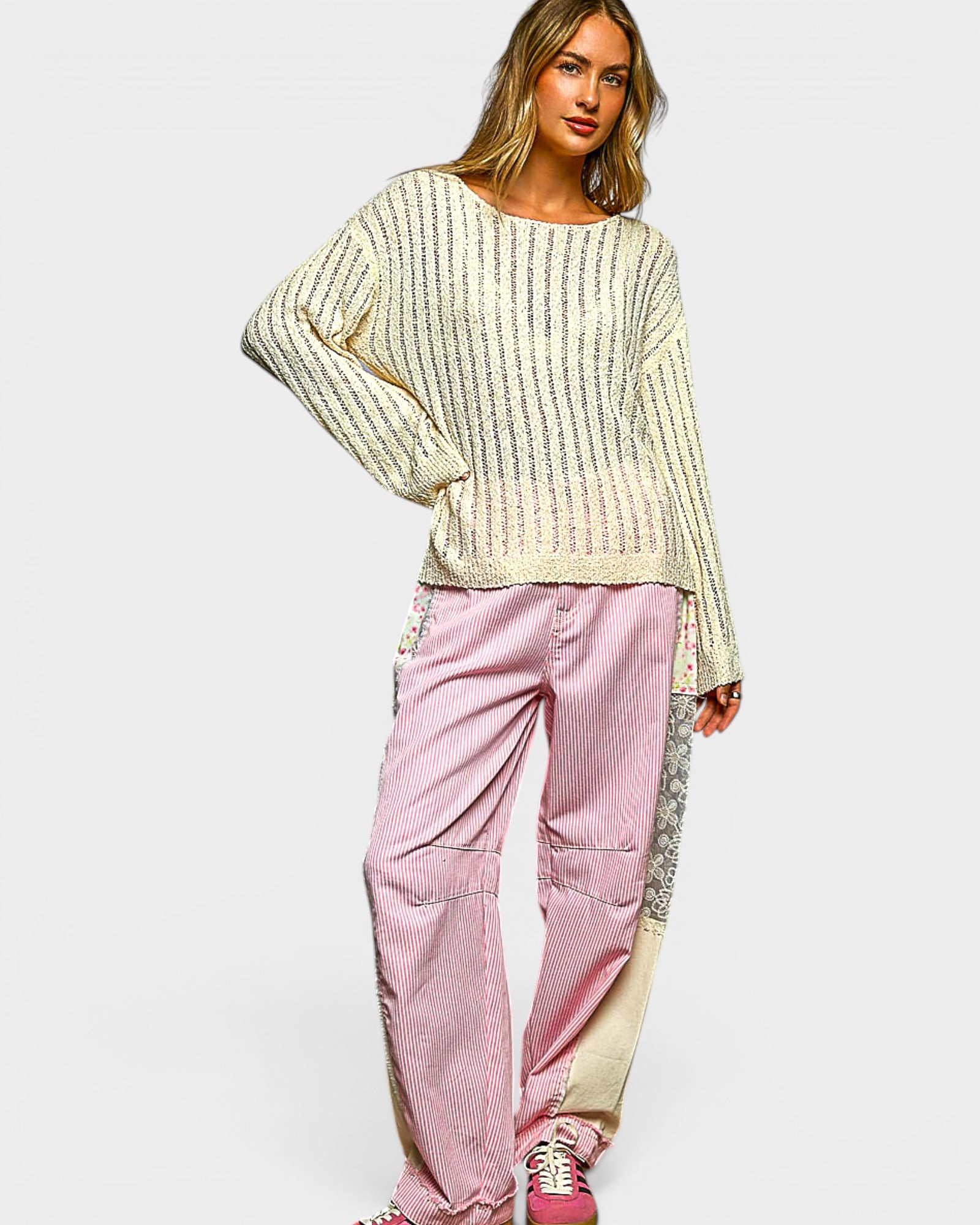 Woman wearing a cream sweater and pink pants on a white background
