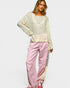Woman wearing a cream sweater and pink pants on a white background