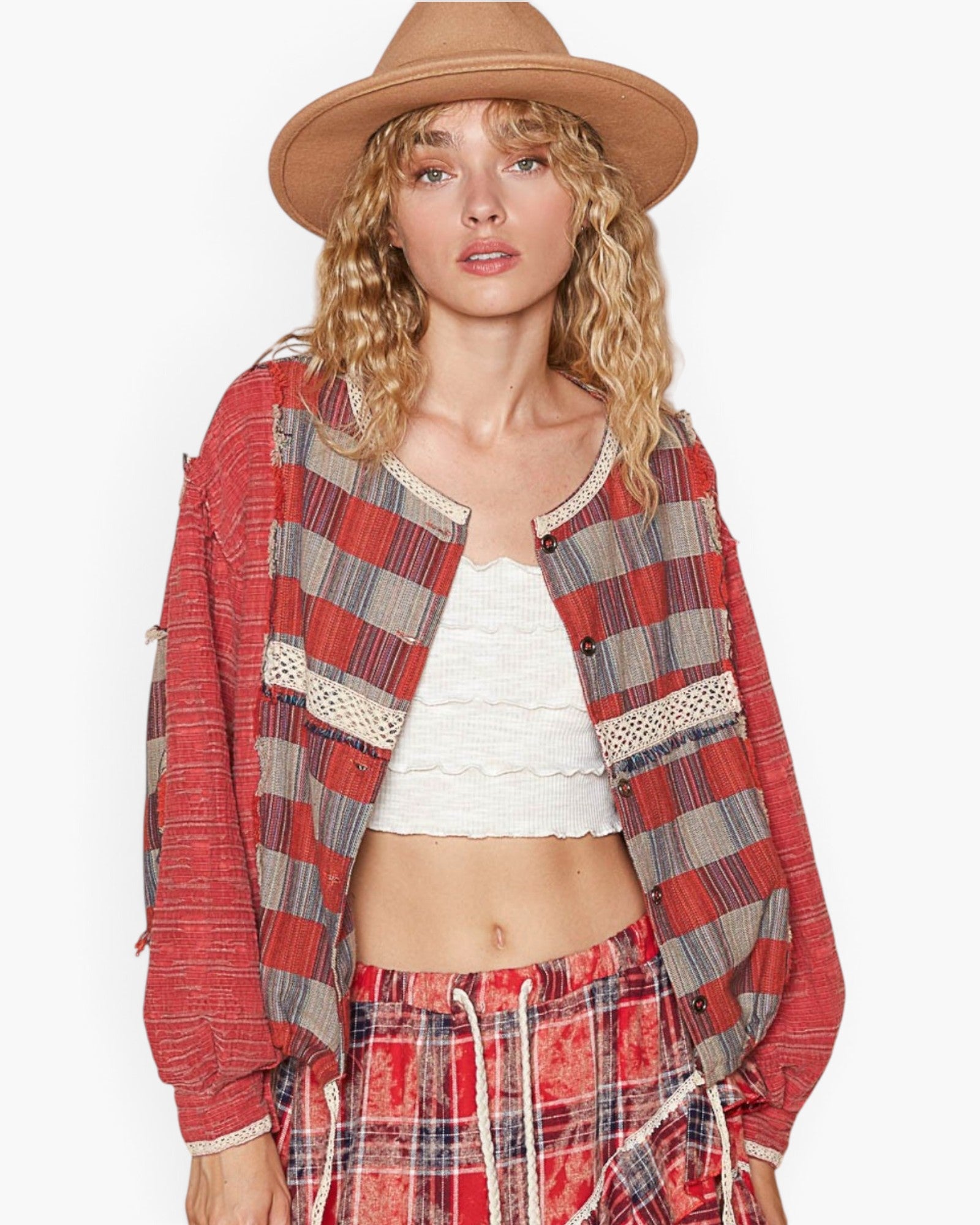 A woman modeling a bohemian-style red plaid jacket with lace trim, a white ribbed crop top, matching red plaid pants, and a tan wide-brim hat against a plain white background.