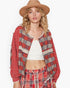 A woman modeling a bohemian-style red plaid jacket with lace trim, a white ribbed crop top, matching red plaid pants, and a tan wide-brim hat against a plain white background.