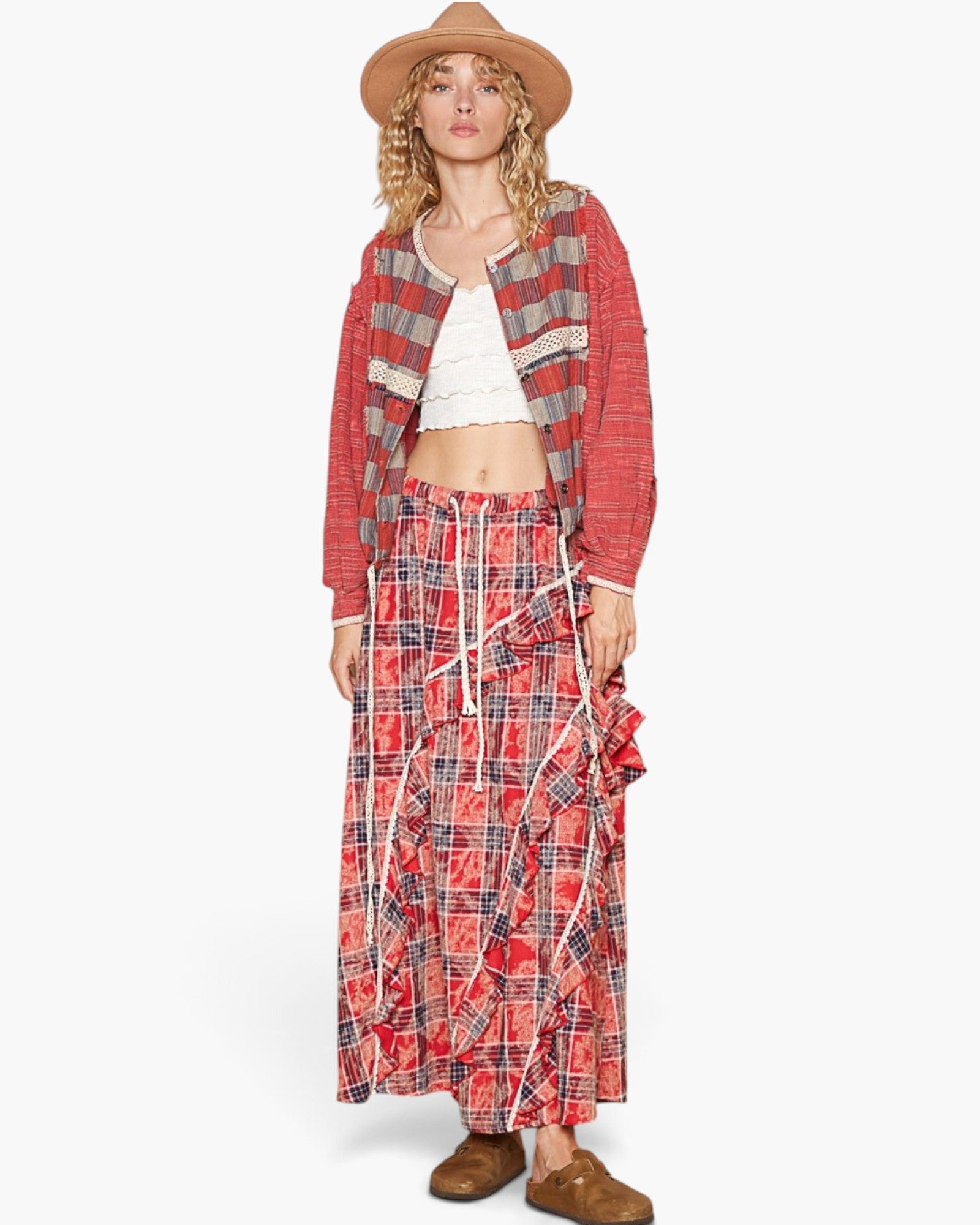 A model wearing a red and gray plaid cardigan, a matching long pleated skirt, a white crop top, and a tan wide-brim hat, standing against a light gray studio background.