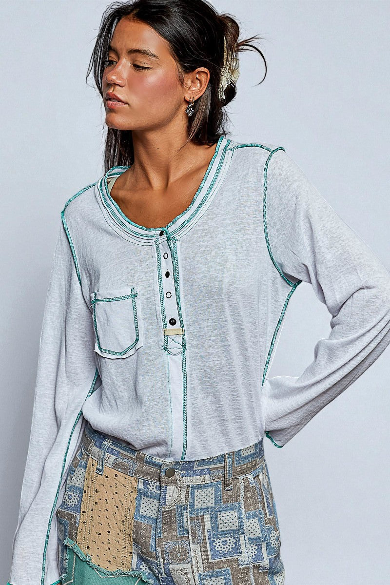 Woman wearing a light gray long-sleeve shirt with green accents and patterned pants on a plain background