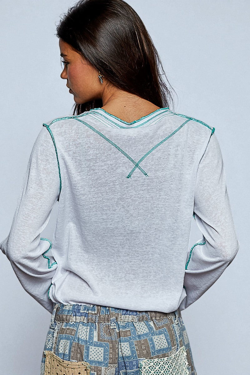 Woman wearing a light gray long-sleeve top with teal accents on a plain background