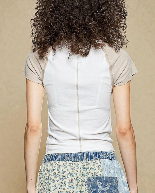 Person wearing a white top with beige sleeves and a patterned blue skirt on a beige background