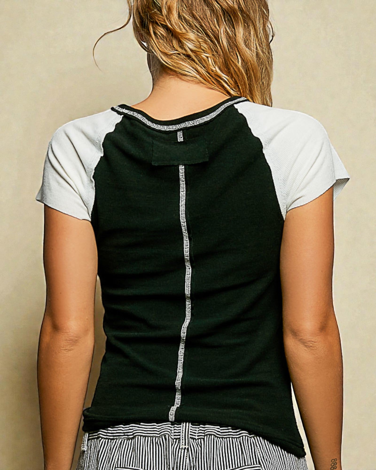 Person wearing a black and white sleeveless top with a beige background