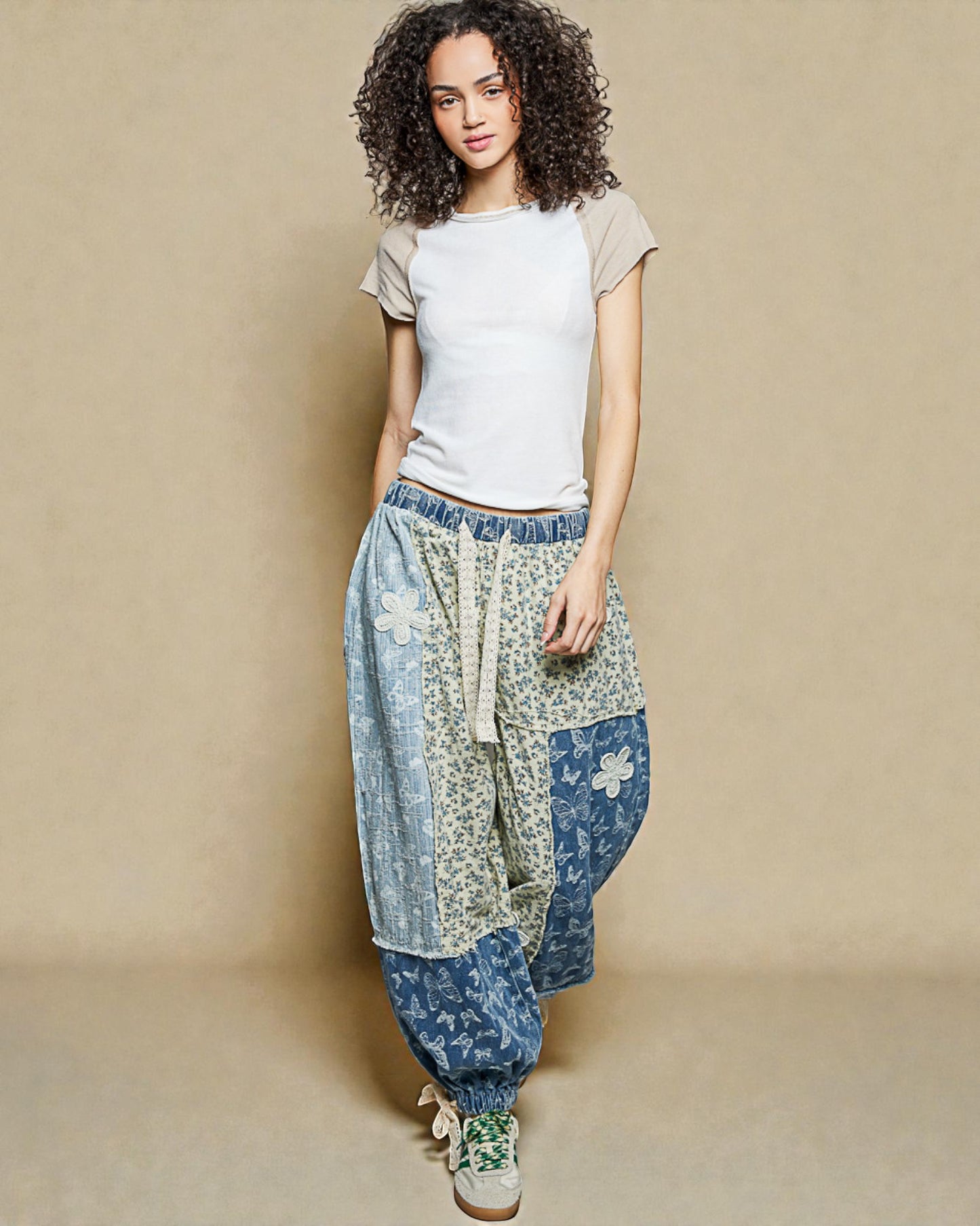 Woman wearing a white t-shirt and floral patchwork pants on a beige background
