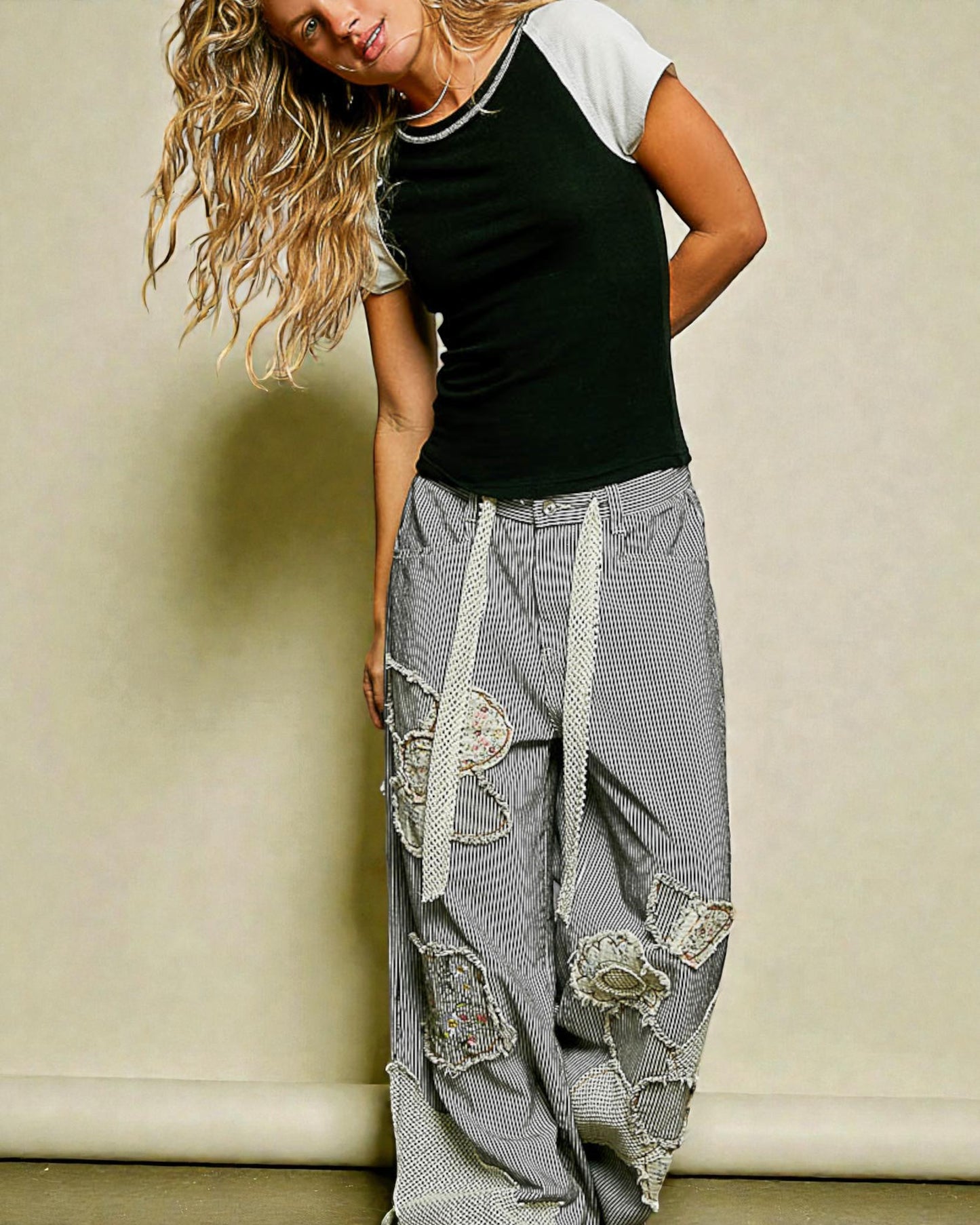 Woman wearing a black top and gray patchwork pants against a beige wall.