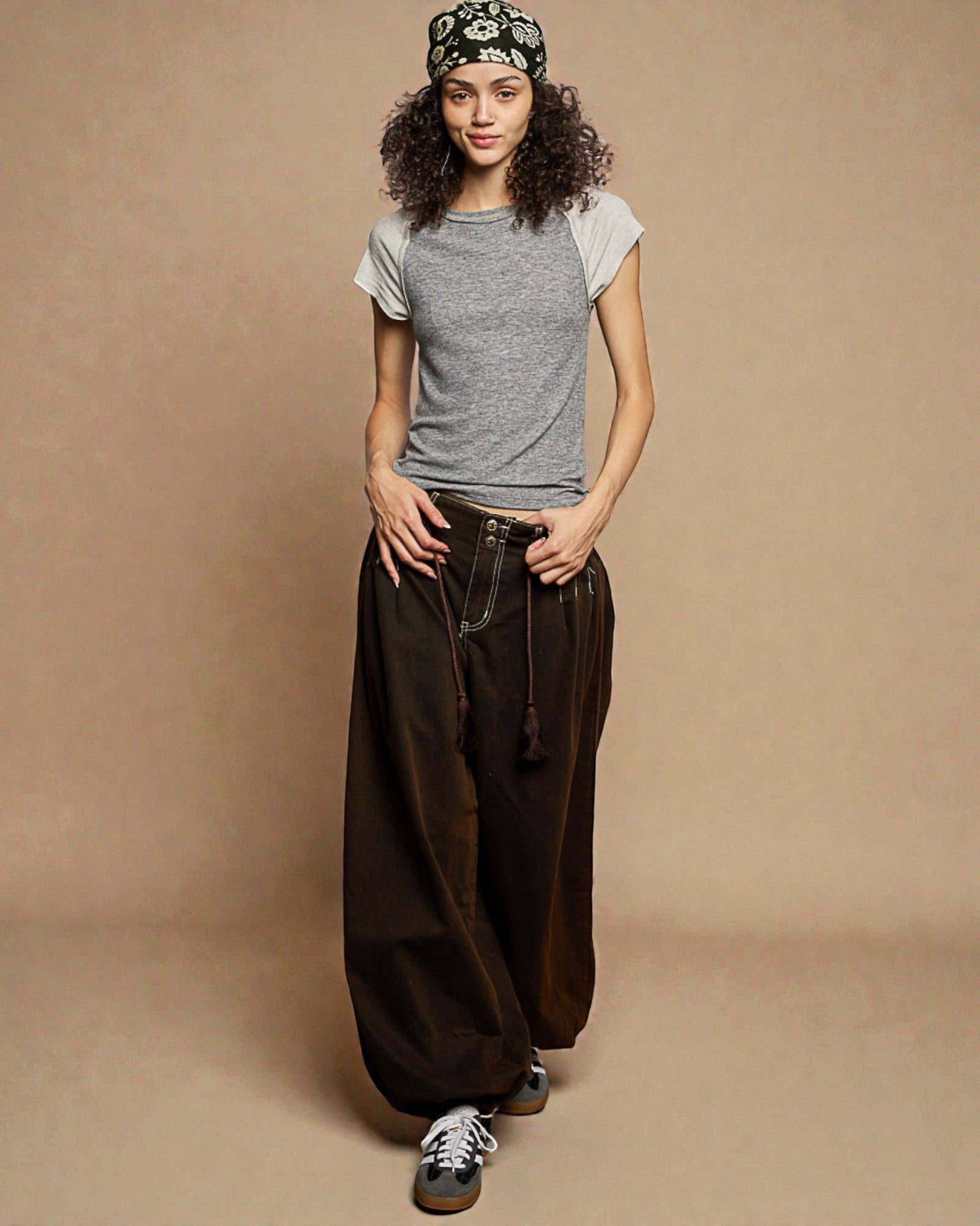 Woman wearing a gray t-shirt and dark brown wide-leg pants on a beige background