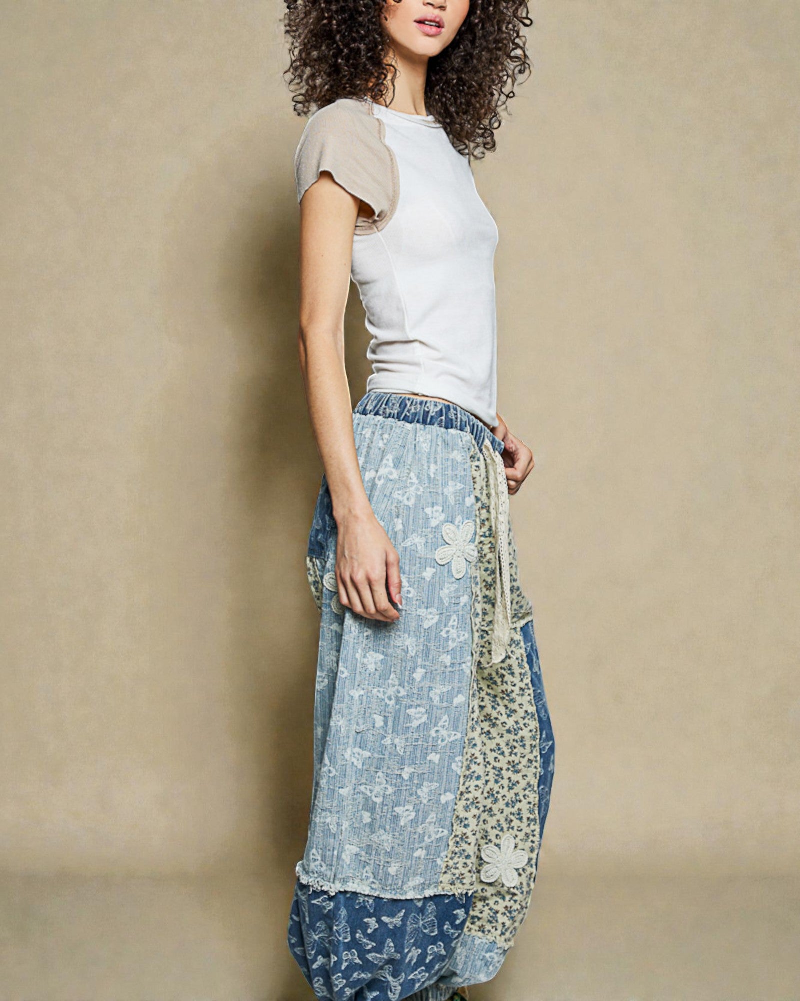Woman wearing a white top and floral-patterned blue pants against a beige background