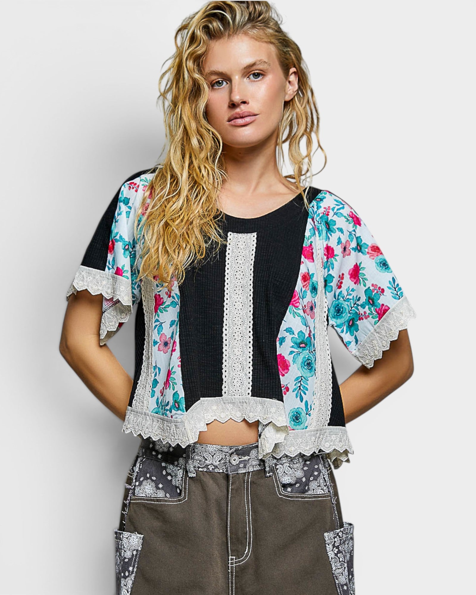 Woman wearing a floral kimono over a black top with a white lace trim on a plain background