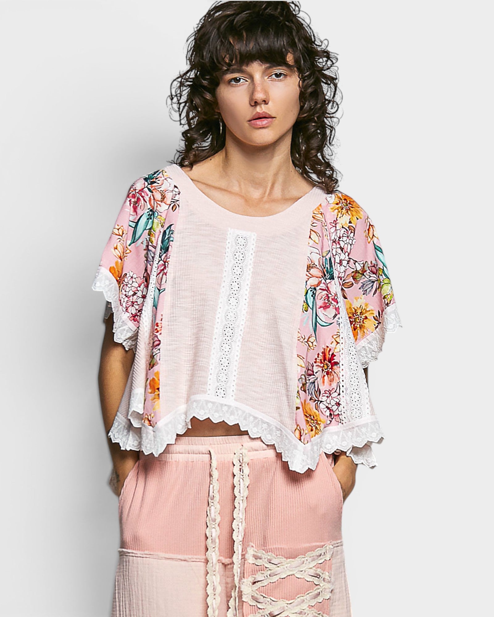 Woman wearing a floral kimono over a pink top and pants on a white background