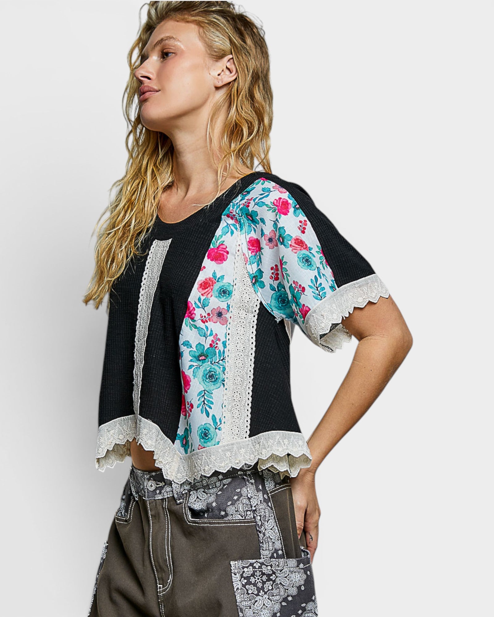 Woman wearing a black top with floral sleeves and lace trim on a white background