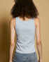 Person wearing a light blue tank top and jeans against a beige background