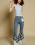Woman wearing a light blue sleeveless top and denim bell-bottom pants with lace trim on a beige background