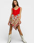 Woman wearing a red top and floral skirt with white cowboy boots on a white background